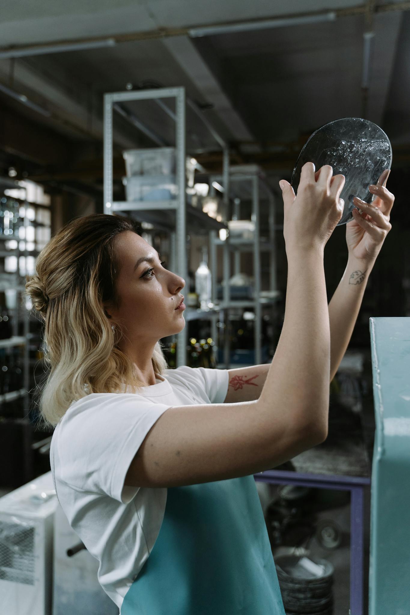 A woman carefully examines a metal disc in an industrial workshop setting.